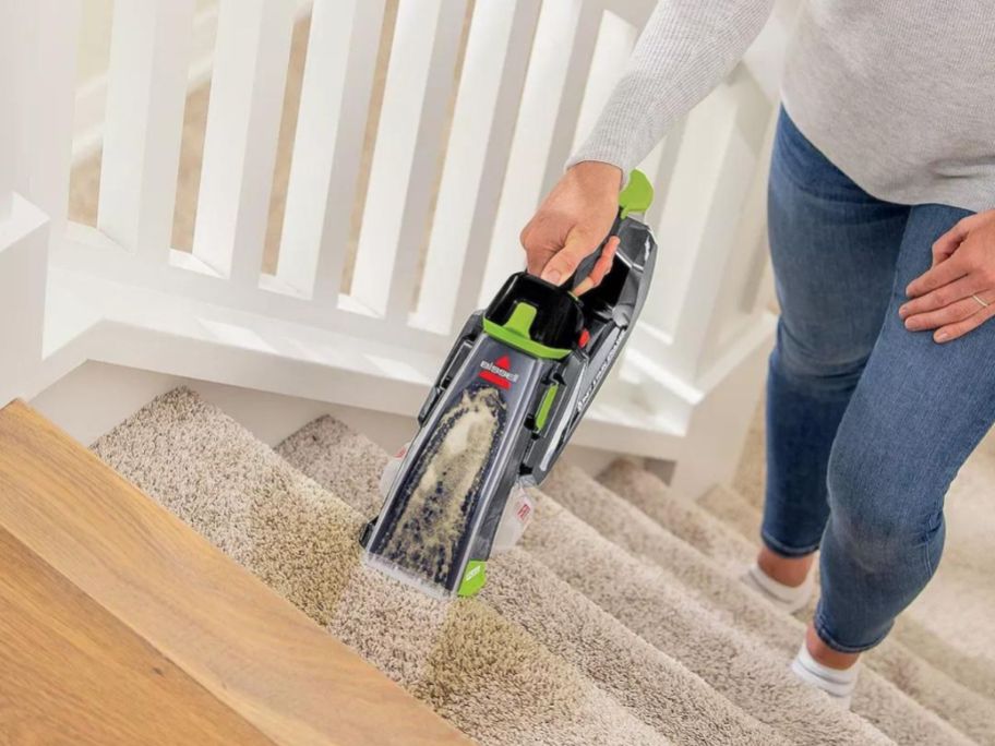 A woman using a Bissell Cordless Pet Vac to clean a stain on the stairs