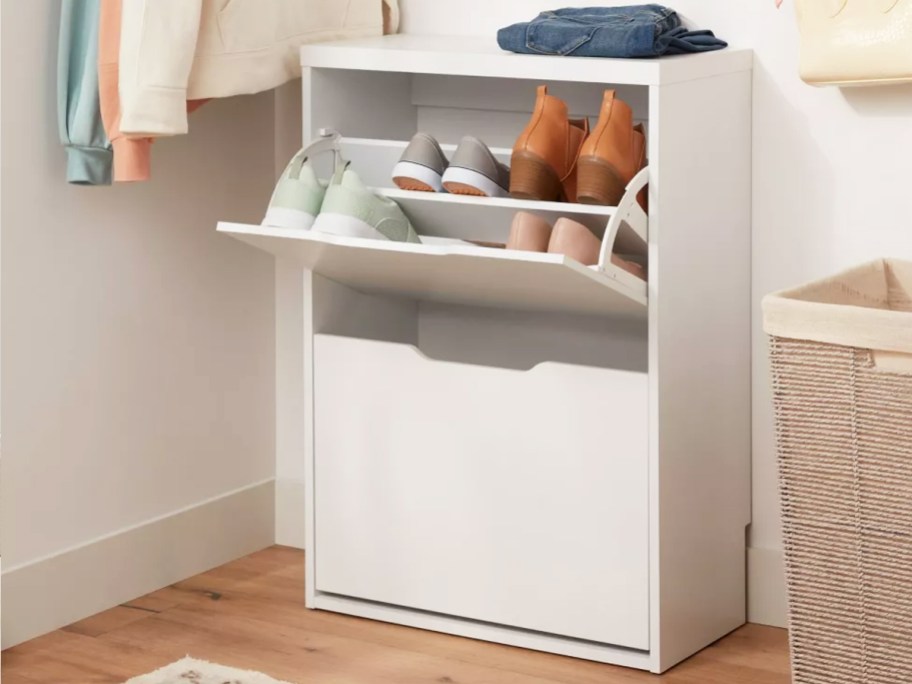 white shoe cabinet with top drawer opened with multiple pairs of shoes inside