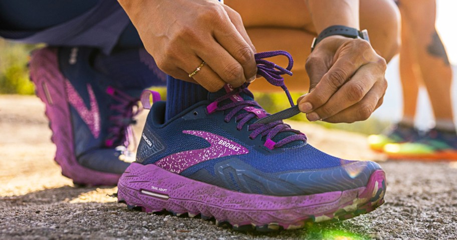 woman kneeling down to tie blue and purple brooks running shoe