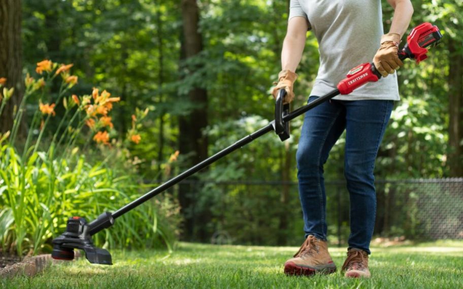 a woman using a cordless weed eater to trim a lawn
