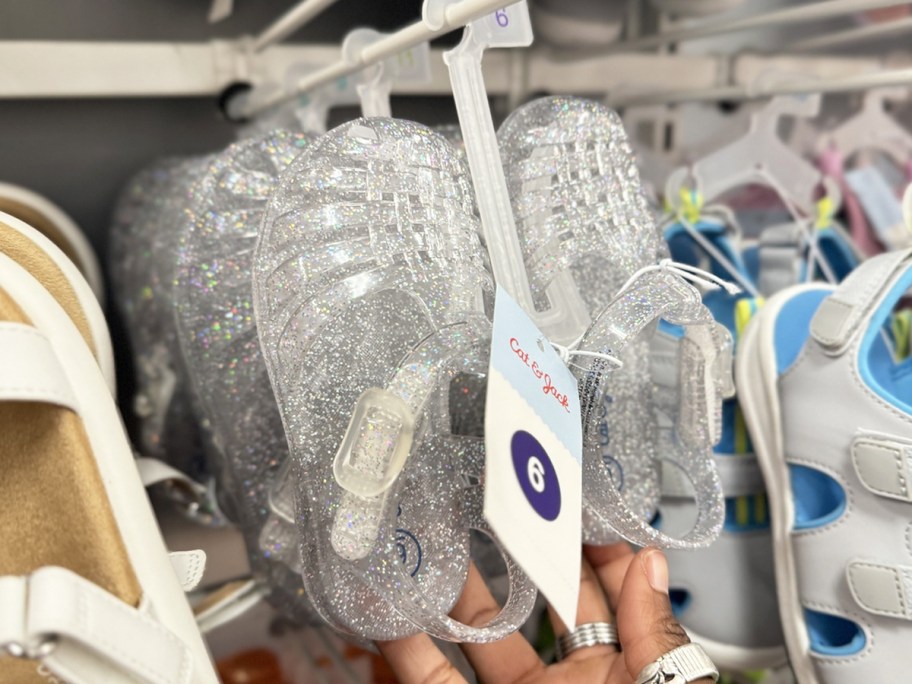 hand touching a pair of sparkly jelly sandals on display rack at target