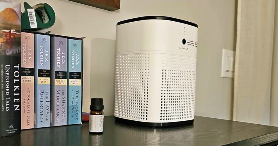 white air purifier and bottle of essential oil on table near books