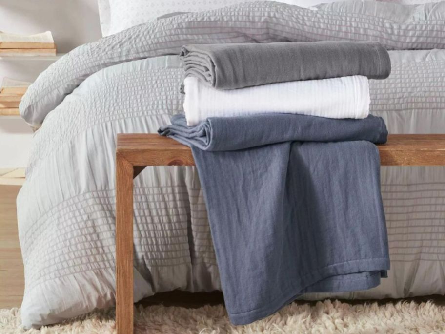 A bed with 3 Clean Spaces 100% Cotton Gauze Bed Blankets folded on a bench