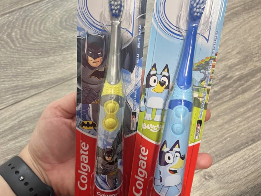 hand holding two Colgate Kids Battery Powered Toothbrushes in batman and bluey prints