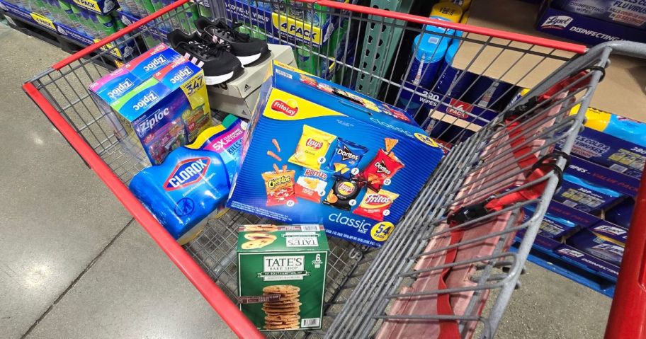 A costco shopping cart filled with Frito Lay chips, Tate Bake shop Cookies, Adidas Sneakers, Clorox Wipes, and Ziploc Bags