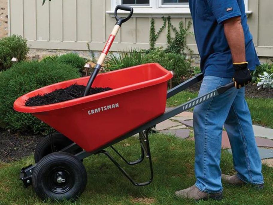 man using a Craftsman wheelbarrow outside with it filled with dirt and a shovel
