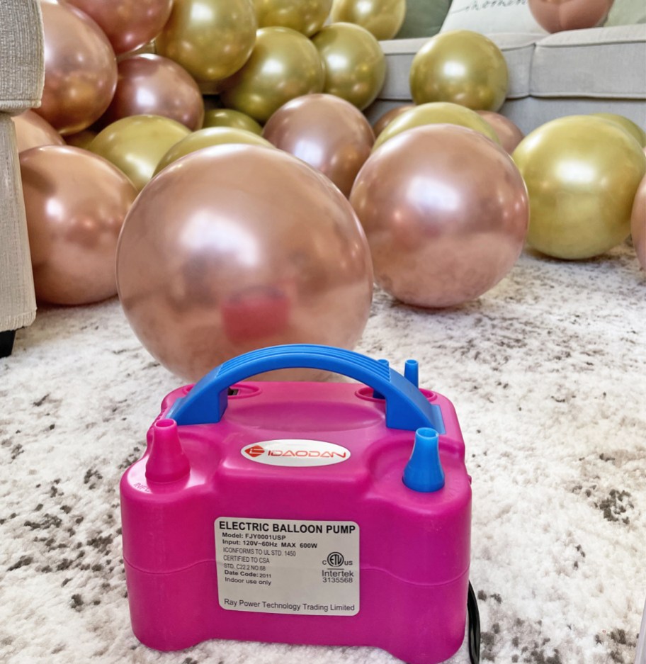 pink and blue balloon pump on floor in front of gold balloons