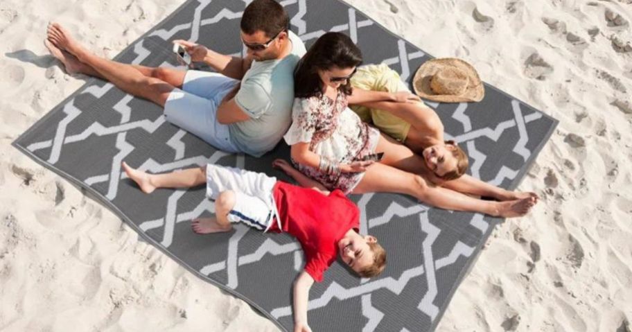 A family lying on an Etta Avenue Aldo Reversible Gray White on the beach