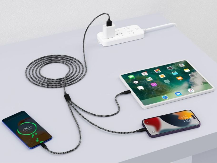 A desk with a firsting charging cable on it charging two phones and a tablet