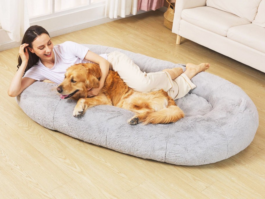 woman and golden retriever laying together in large dog bed