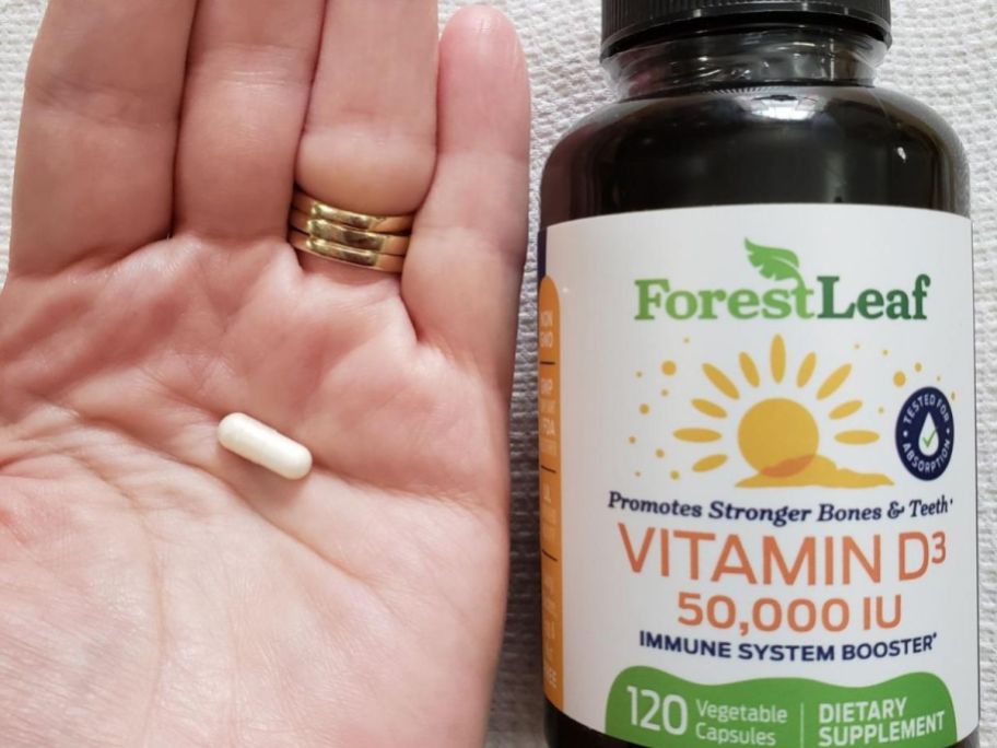 Hand holding a ForestLeaf Vitamin D3 capsule next to a bottle