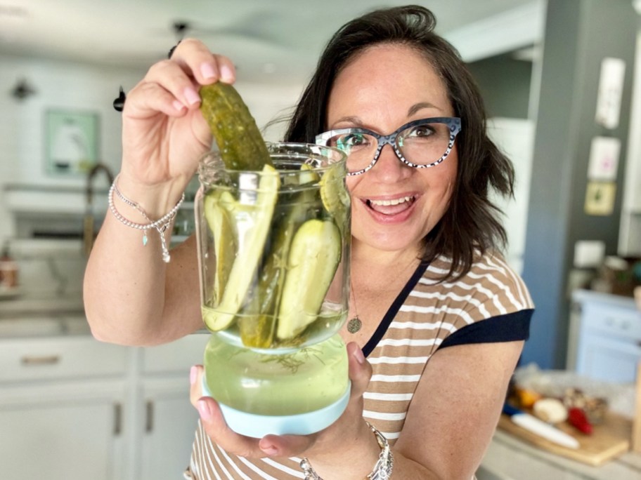 woman holding up a glass pickle jar and grabbing pickle out of from it