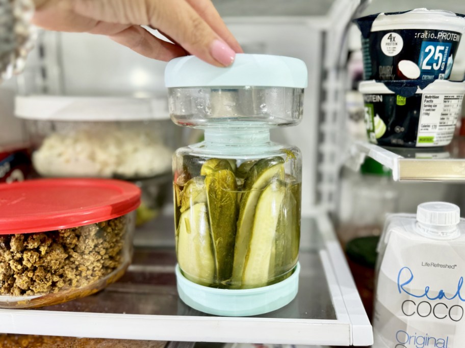 hand touching a glass pickle jar in refrigerator