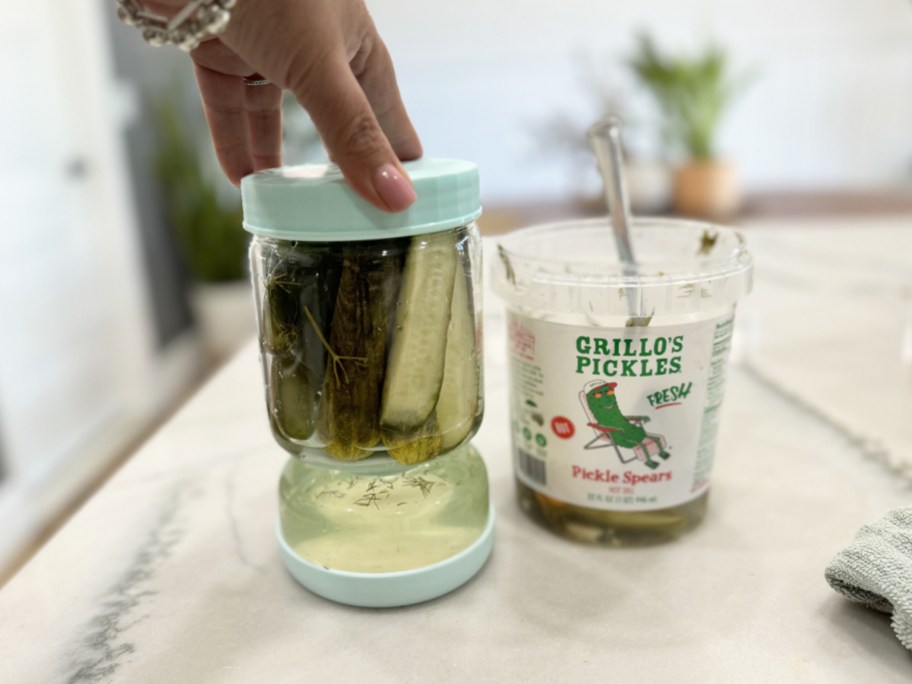 hand touching a glass pickle jar next to a container of grillos pickles