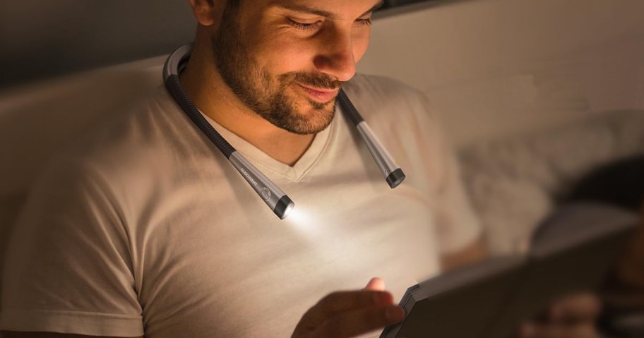 man using a neck light to read a book in bed