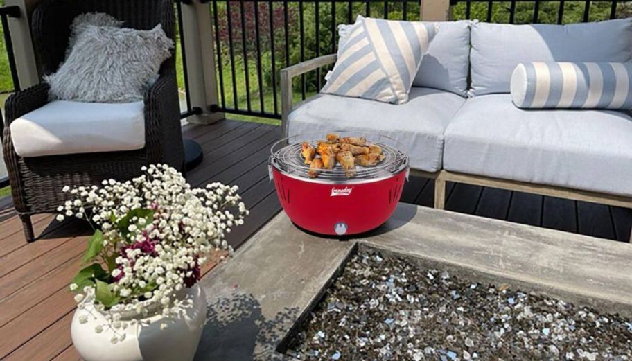 a small red table top grill on a patio next to an outdoor sofa