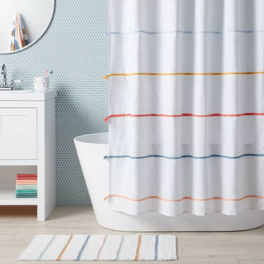 white and multi color stripe and tassel shower curtain and bath mat in bathroom