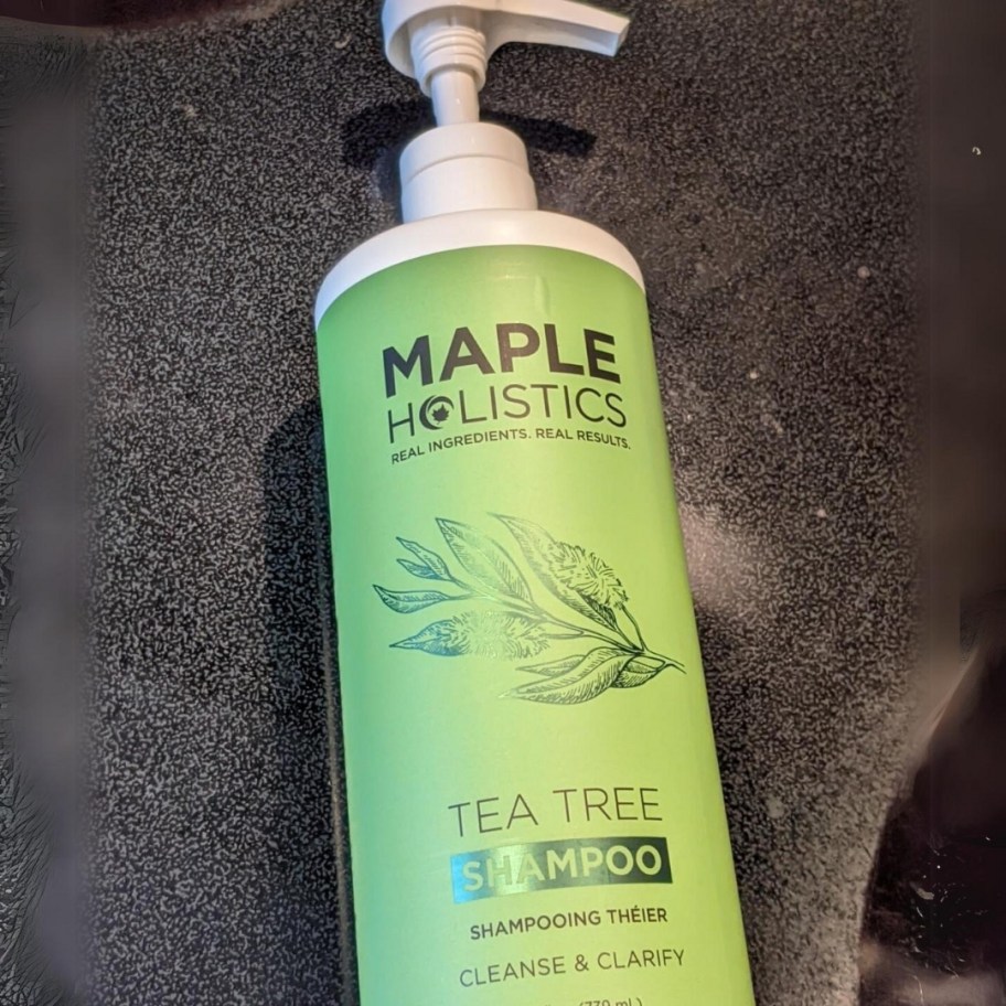 large bottle of Maple Holistics Tea Tree Oil Shampoo with a pump laying on a black background