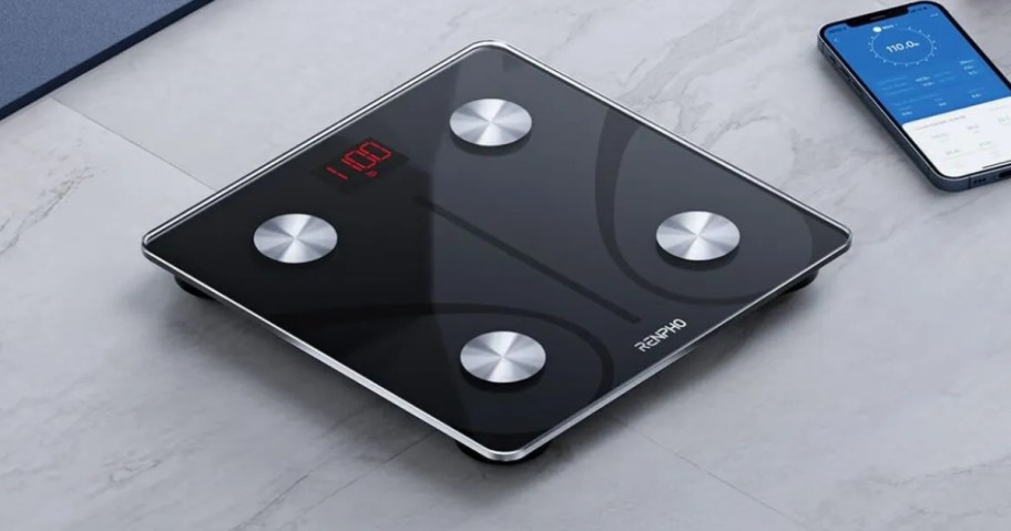 black and silver smart body scale on the floor next to a smartphone