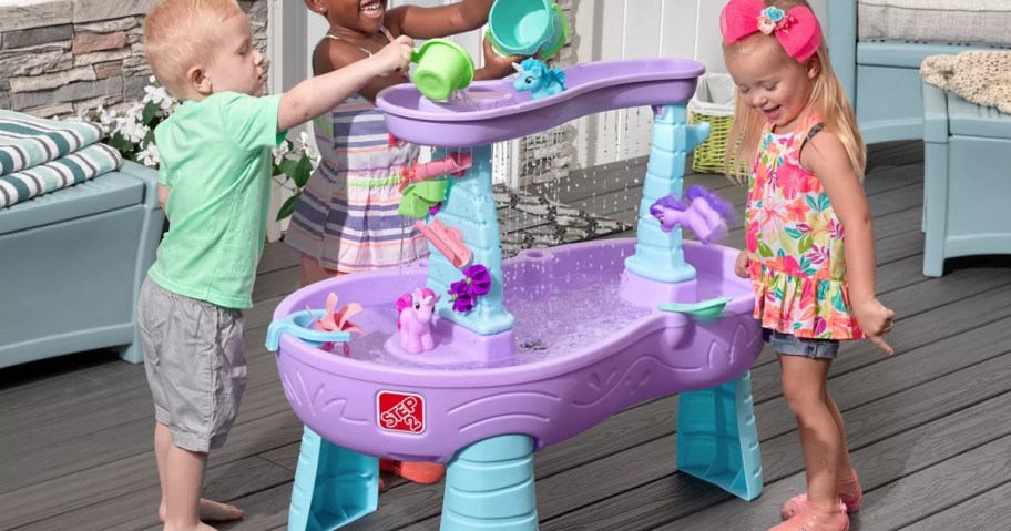 kids playing with a purple and blue Step2 Water Table on a back deck