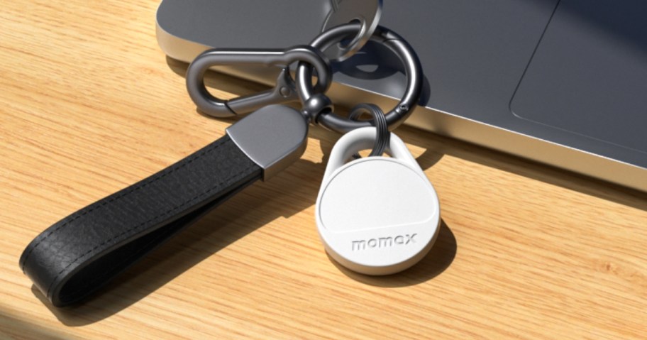 white Momax tracker tag on a black leather keychain laying by a laptop