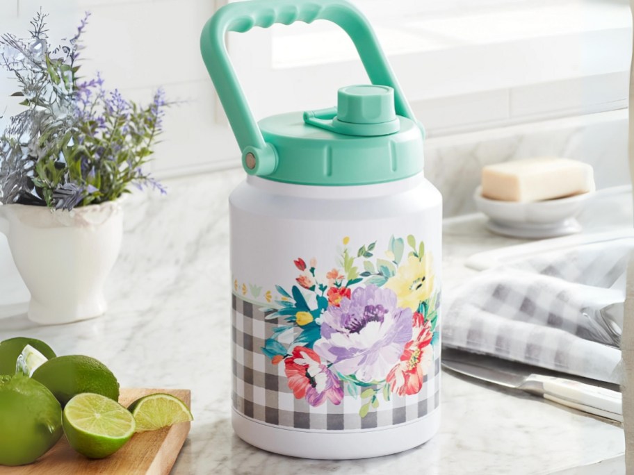 Pioneer woman large water jug with black gingham and flowers and a teal handle on a kitchen counter
