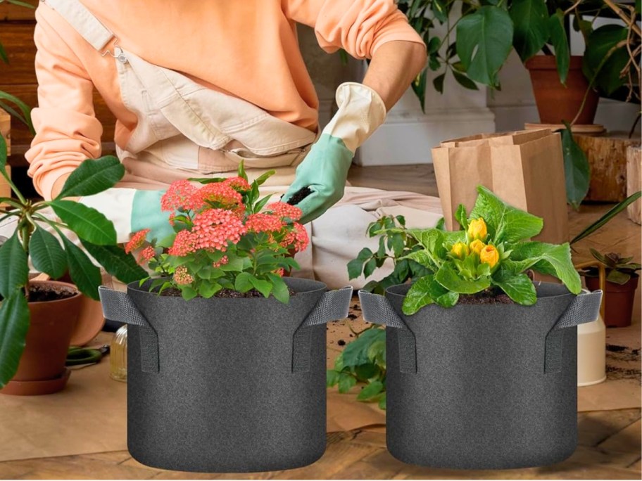 a woman putting pants into black fabric grow bags that are sitting on a wooden table