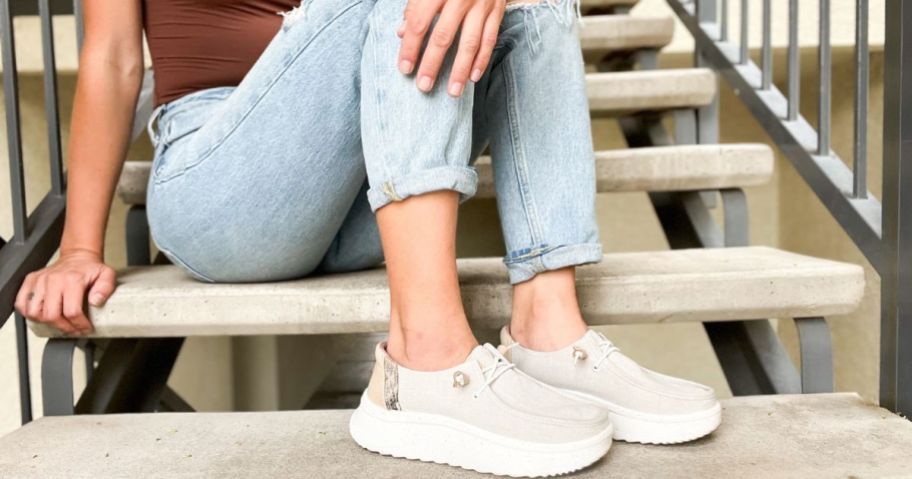 Woman sitting on steps wearing HEYDUDE shoes