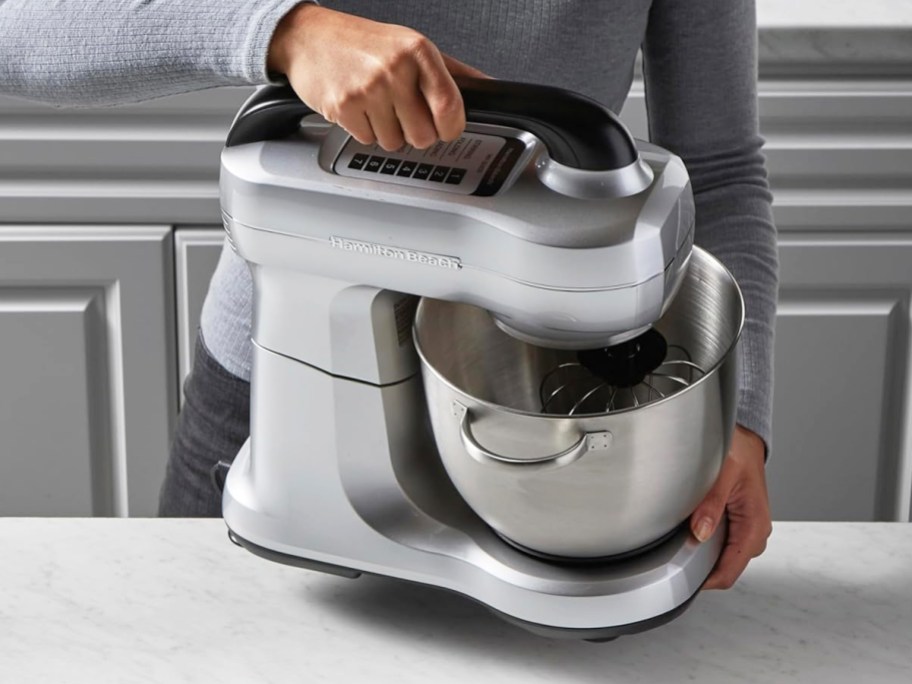 woman lifting silver stand mixer from counter
