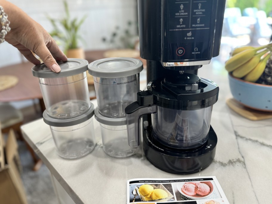 Hand holding pints from the Ninja cream next to the machine and the recipe book