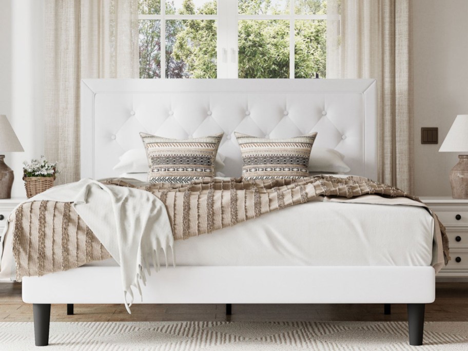 A cozy bedroom features a white tufted bed with patterned pillows and a beige throw.