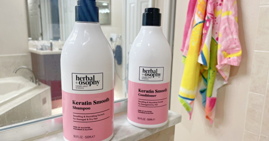 Bottles of Herbalosophy shampoo and conditioner on bathroom counter near mirror