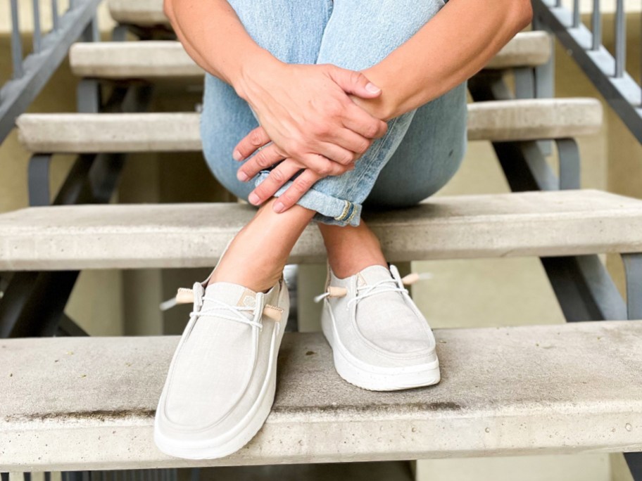 woman sitting on stairs wearing jeans and hey dude shoes