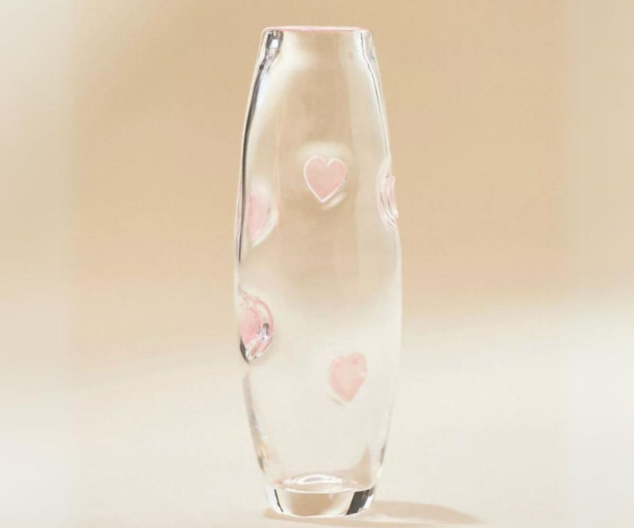 a tall thin clear glass vase with a pink glass heart motiff