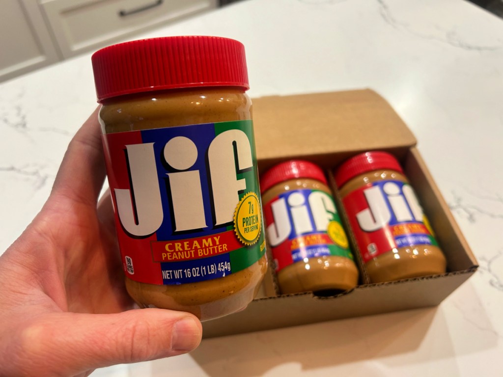 person holding jar of jif creamy peanut butter in kitchen