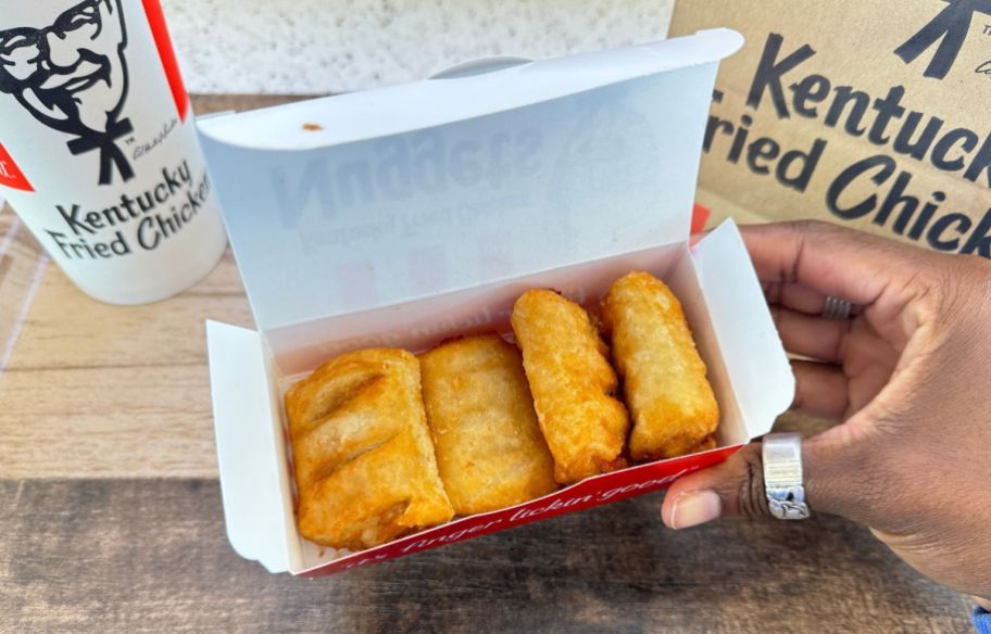 A womans hand holding a 4 piece box of KFC apple pie poppers