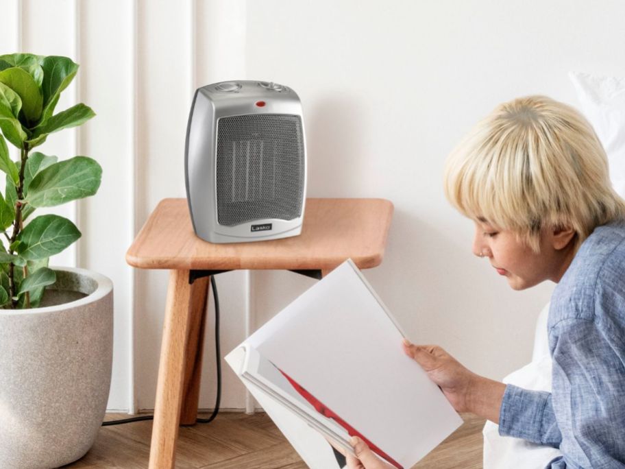 person reading beside Lasko Electric Ceramic Space Heater sitting on tv tray