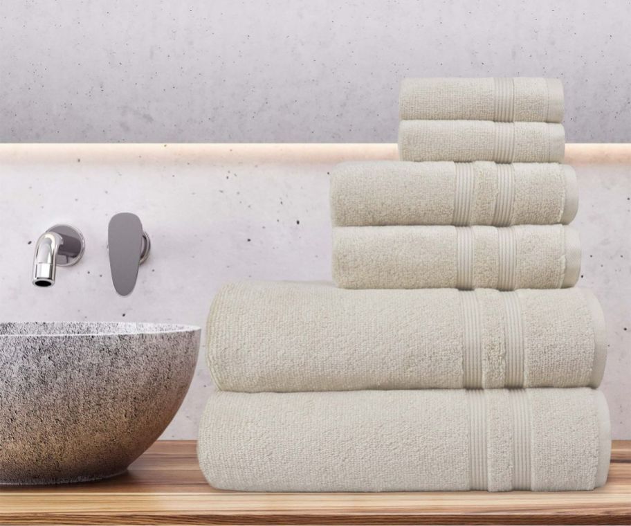 a stack of towels and washcloths in beige folded on a bathroom counter.