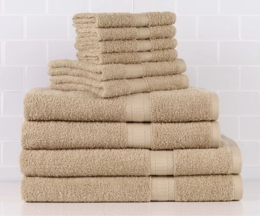 a stack of towels and washcloths in tan folded on a bathroom counter.