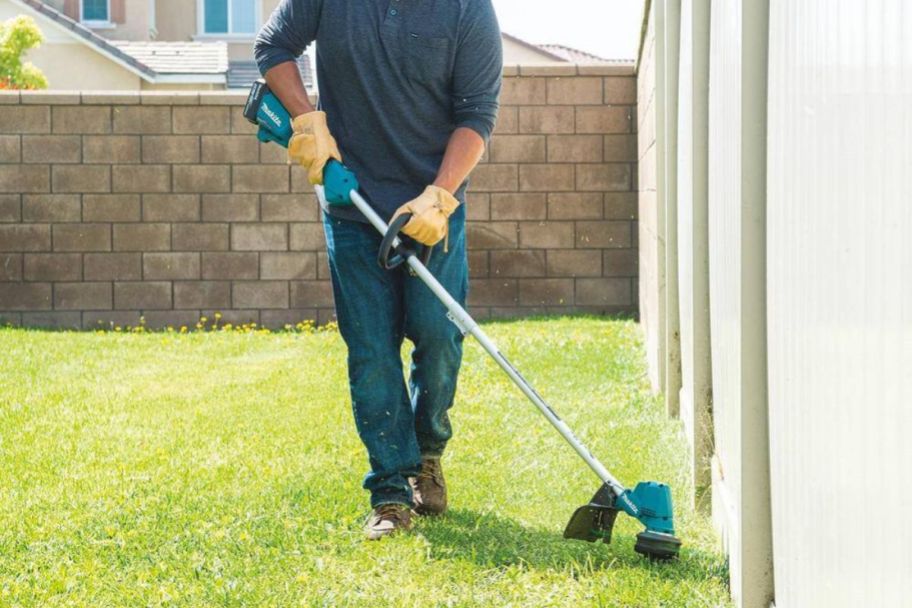 a man weedeating next to a house with a string trimmer