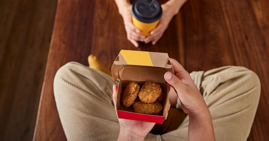 person sitting on floor holding box of chicken nuggets