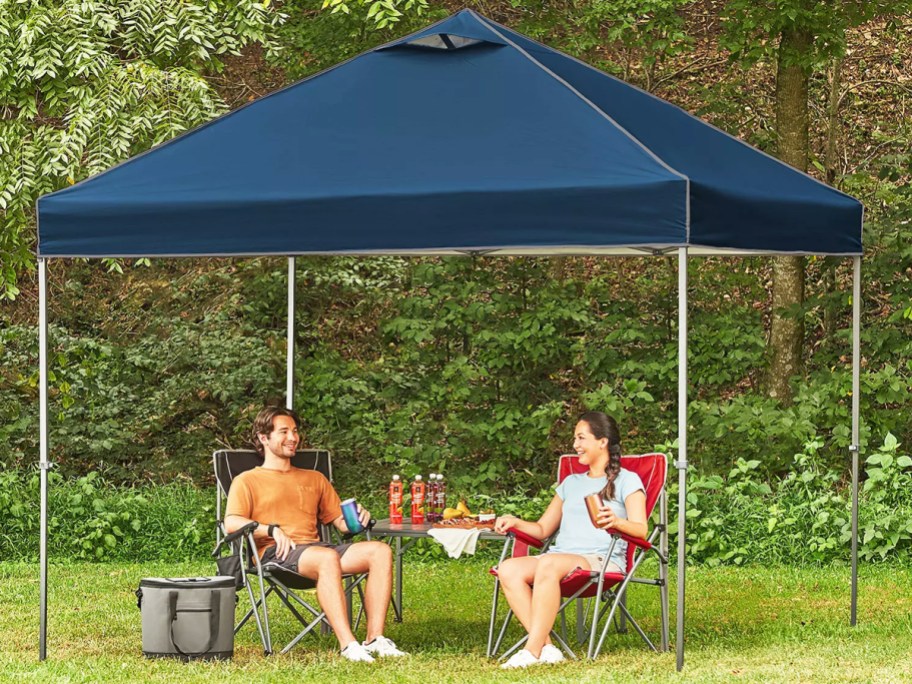 two people sitting under a blue pop up canopy