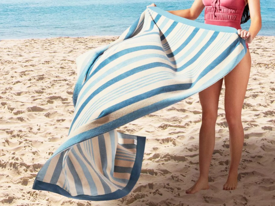 woman placing a blue and white striped towel on sand at beach