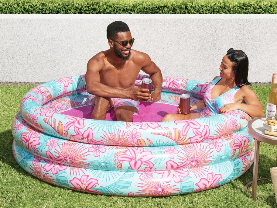 man and woman sitting in tropical print inflatable pool