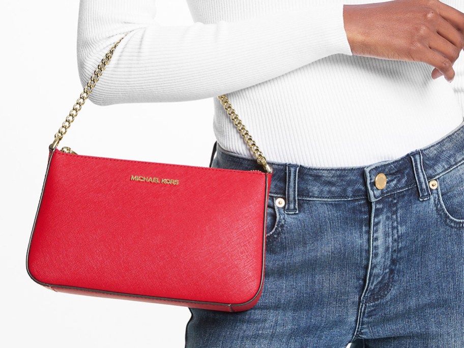 woman in white shirt and jeans with red michael kors bag