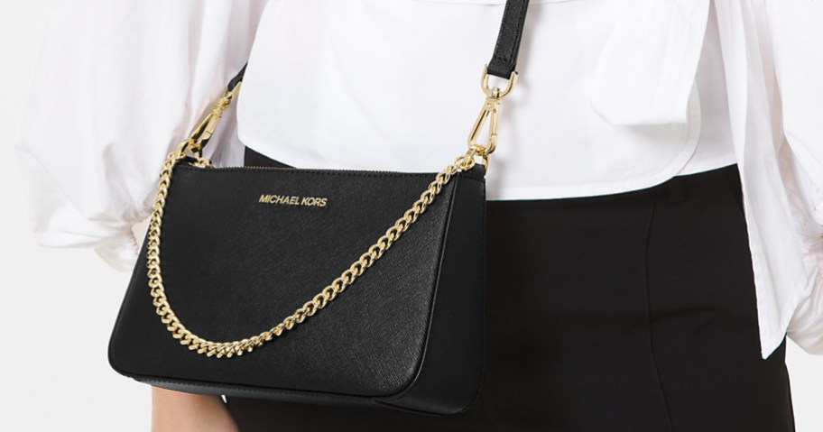 woman with a black micheal kors crossbody bag with gold chain hanging front front