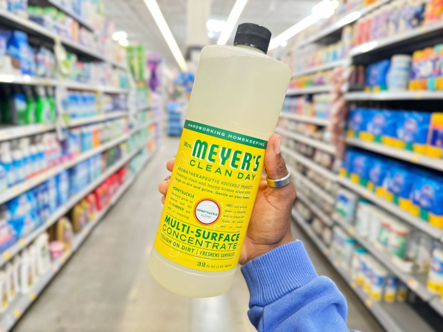 A hand holding a Mrs. Meyer's 32oz Multi-Surface Concentrate bottle in Honeysuckle