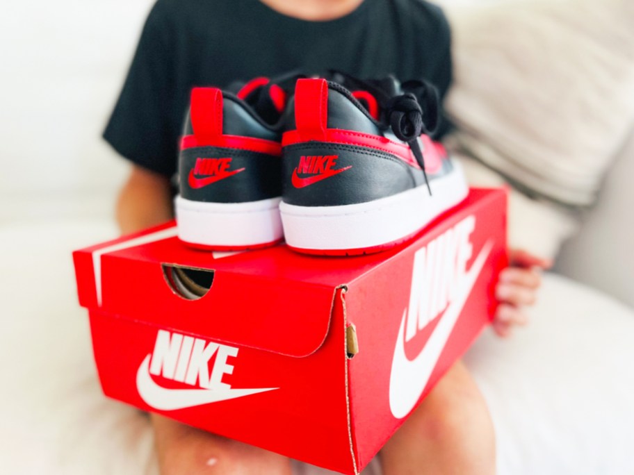 holding a pair of nike sneakers on top of red nike shoe box