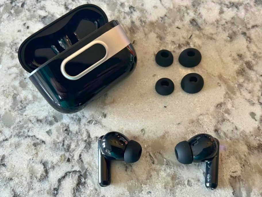 black wireless earbuds, charging case and extra tips on a granite countertop