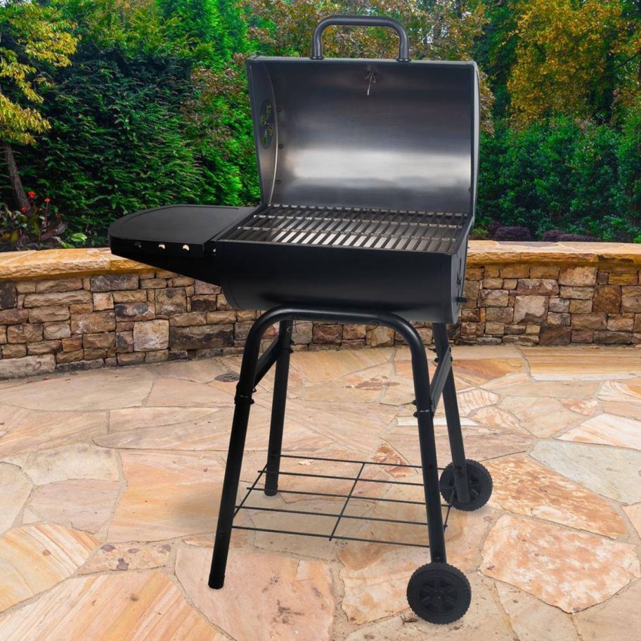 a black smoker grill on a patio with the lid raisede